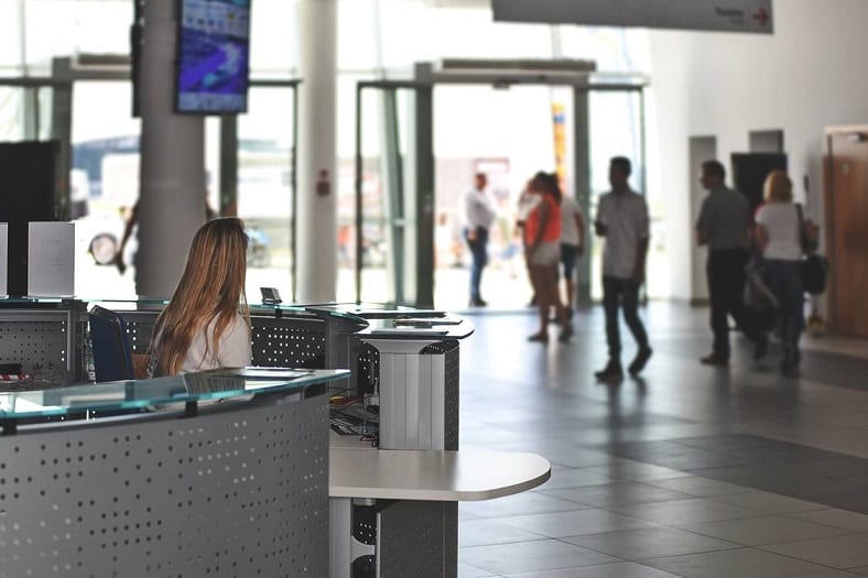 A receptionist looking at people in the background walking on a grey tiled floor. 